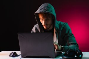 Professional hacker with laptop sitting at table on dark background